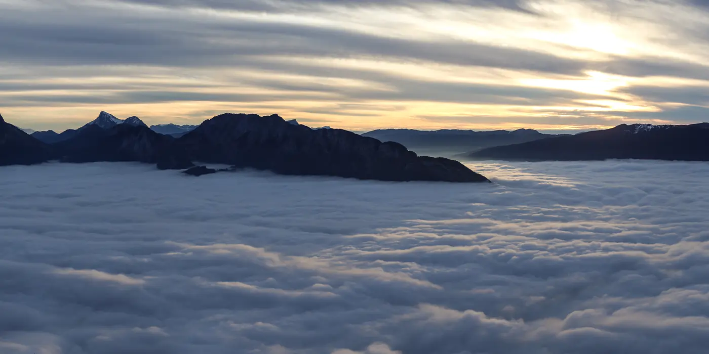 Reliefs du massif des Bauges au-dessus d’une mer de nuages dans la lumière du soir.